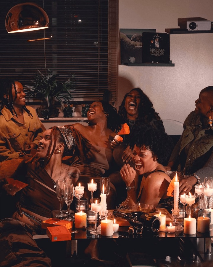 Friends laughing together at a candlelit table, from The Skin Deep.